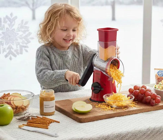 Child safely cranking Geedel Rotary Cheese Grater to shred cheese, snowy winter day outside window, cozy snow-day kitchen scene 